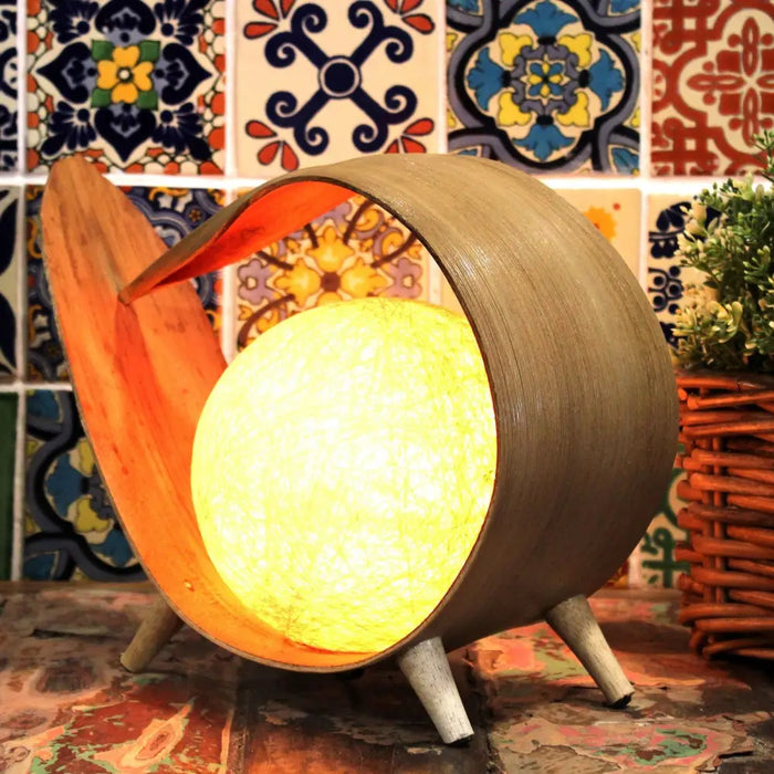 Natural coconut lamp with a warm glowing spherical light encased in a curved wooden frame with orange lining and three legs