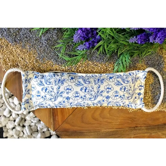 A cream cotton heating bag with blue floral pattern and braided handles filled with natural wheat for warmth