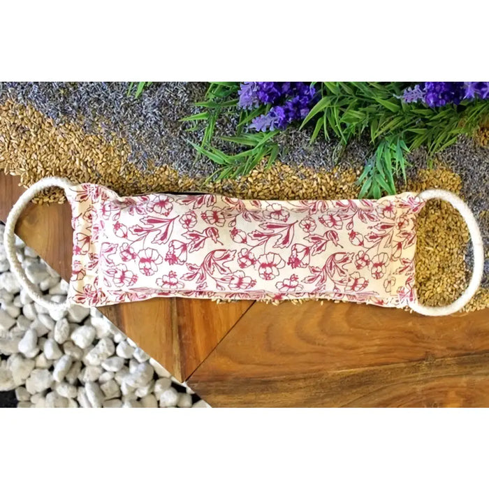 A cream cotton face mask with pink floral pattern and white ear loops shown alongside natural cotton and wheat heating bags purple
