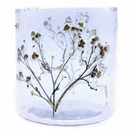 A clear recycled glass candle holder with a straight design holding a dried brownish babys breath sprig inside