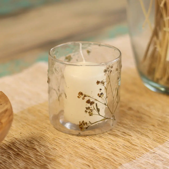 A clear recycled glass candle holder with a white wax candle and dried babys breath flowers inside