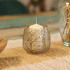 A clear recycled glass candle holder with dried floral designs holding a white pillar candle natural floral pino style