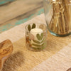 Clear glass candle holder with pressed green and brown leaves made from recycled glass holding a white pillar candle