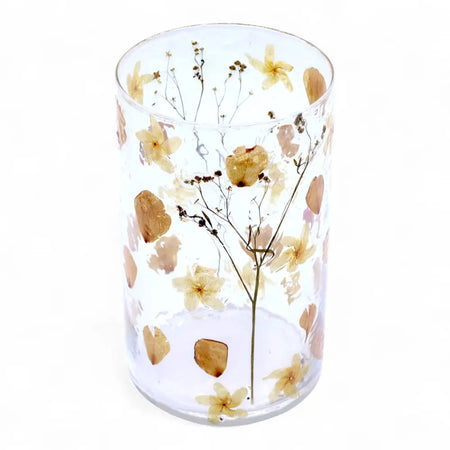 Clear glass cylindrical candle holder vase with embedded dried flowers in soft yellow beige and brown tones made from recycled glass