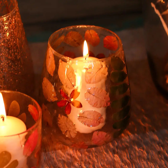 Natural floral glass vase candle holder primavera with a lit white candle in clear recycled glass with dried leaves and flower