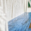 Blue distressed wooden macrame hanging shelves mounted on textured white wall for storage and decor