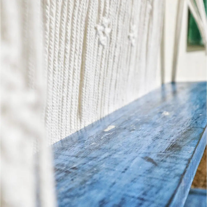 Blue distressed wooden macrame hanging shelves mounted on textured white wall for storage and decor
