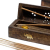 Dark brown natural mango wood smoke box with gold elephant emblem and perforated lid holding light brown incense sticks