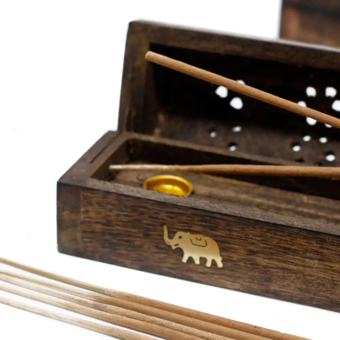 Dark brown natural mango wood smoke box with gold elephant emblem and perforated lid holding light brown incense sticks