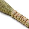 A natural pampas broom with a tightly woven straw handle bound by red twine showing pampas brooms detail
