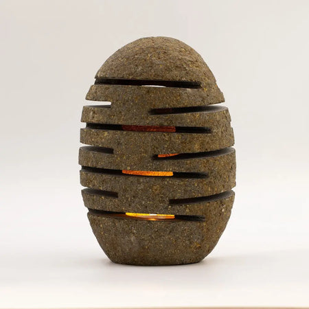 Natural riverstone candle holder shaped like a brown standing stone with slits glowing warm orange light