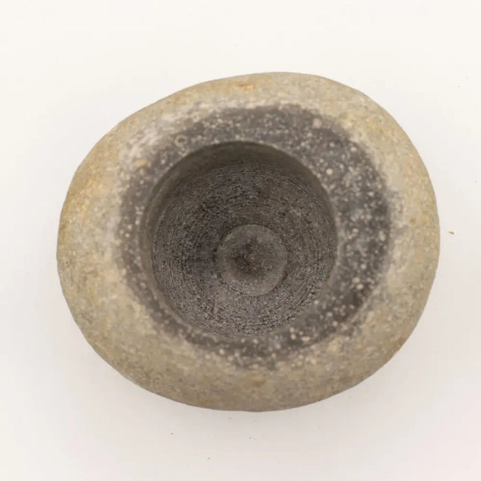 Natural riverstone pestle with a rough gray surface and worn interior in a large natural riverstone mortar