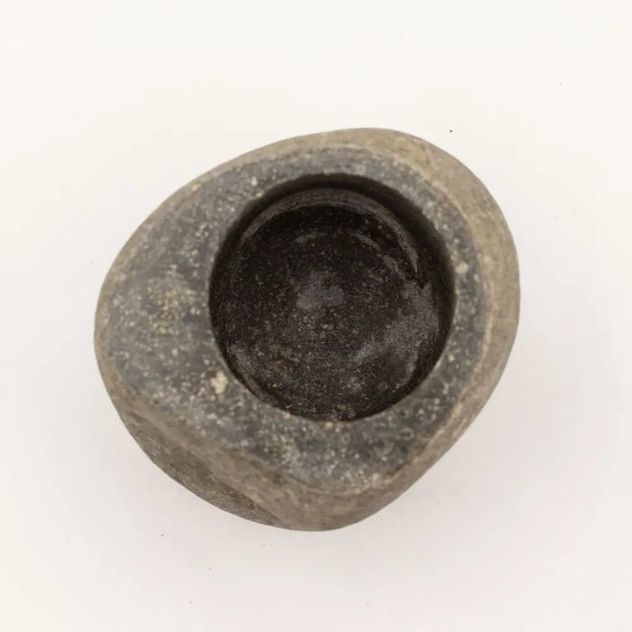 A smooth dark gray natural riverstone pestle mortar with a rounded shape and hollowed center for grinding use