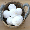 White spherical bath bombs with dried herbs and gold flakes in natural woven seagrass baskets set of 2