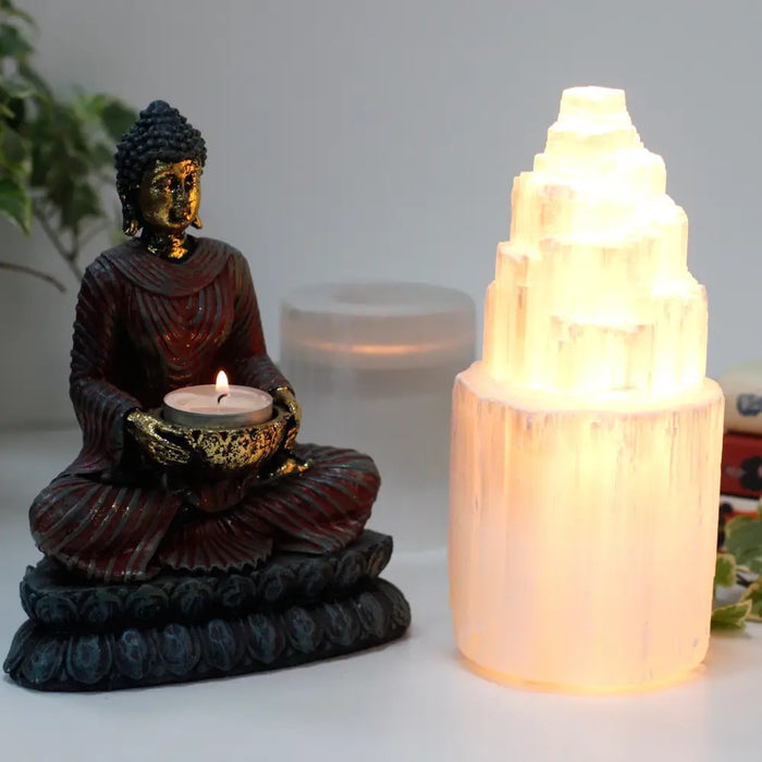 A glowing translucent white natural selenite lamp with a tiered pyramid design shown among three sizes