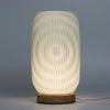 New wave lamp with a softly glowing off-white cylindrical body, vertical ridges, and wooden base for modern decor