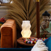 A warm white ceramic new wave lamp with a wavy ribbed design on a wooden table called star twisted