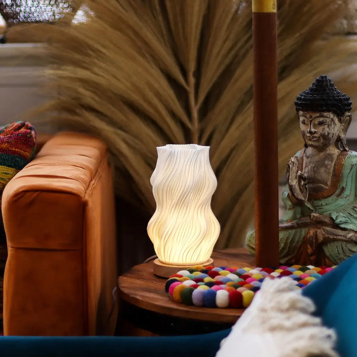 A warm white ceramic new wave lamp with a wavy ribbed design on a wooden table called star twisted