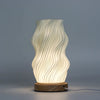 A modern cream ceramic table lamp with wavy ribbed design and wooden base called new wave lamp star twisted