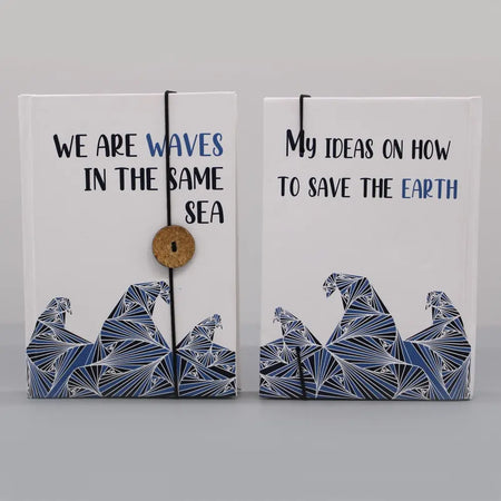 Two white hardcover notebooks with blue wave designs bound by a black cord and wooden button strap called waves in the same sea