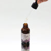 A brown glass bottle of organic hair serum with black dropper cap labeled with ingredients including organic castor and lavender