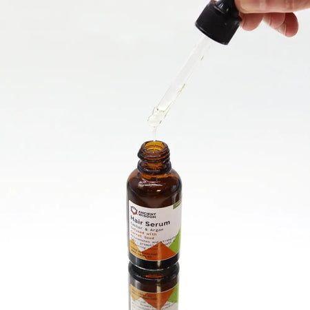 A brown glass bottle of organic hair serum with black dropper labeled castor argan infused with carrot seed 30ml