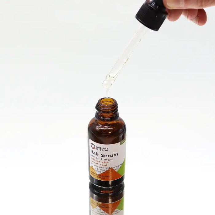 A brown glass bottle of organic hair serum with black dropper labeled castor argan infused with carrot seed 30ml