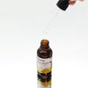 A brown glass bottle of ancient wisdom organic hair serum with black dropper cap and yellow label for organic hair care