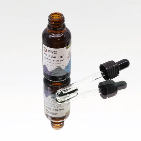 A dark amber glass bottle of organic hair serum with black dropper cap labeled castor and argan ingredients