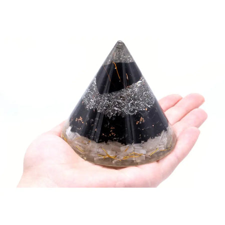 Orgonite cone with selenite and black tourmaline held in hand showing black and clear resin with quartz and gold threads