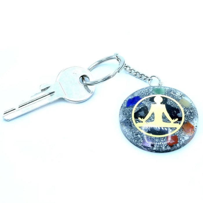 A circular orgonite power keyring with a silver metal ring and colorful gemstone resin around a gold buddha figure