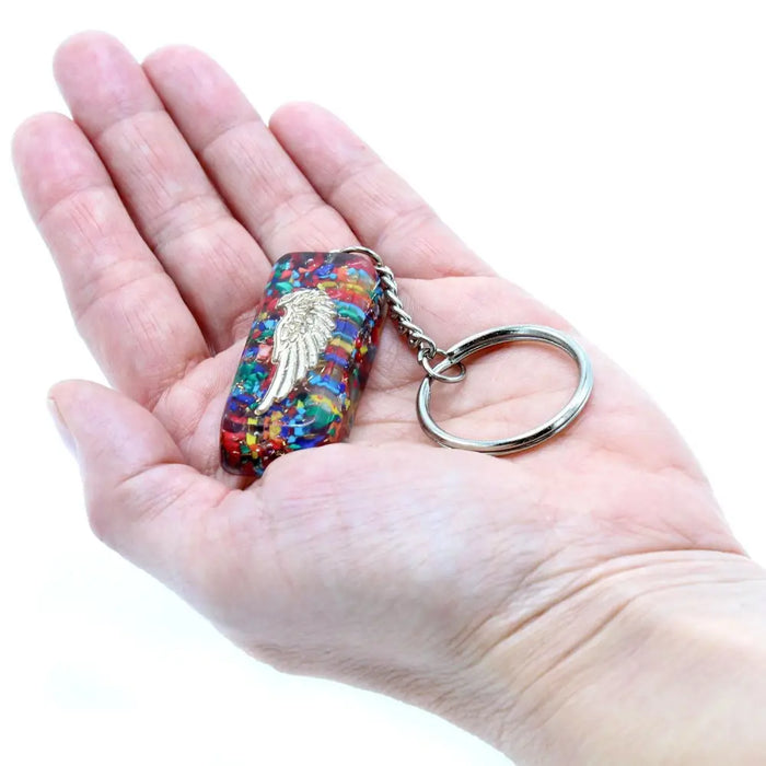 A colorful rectangular orgonite power keyring with a silver angel wing design attached to a metal ring