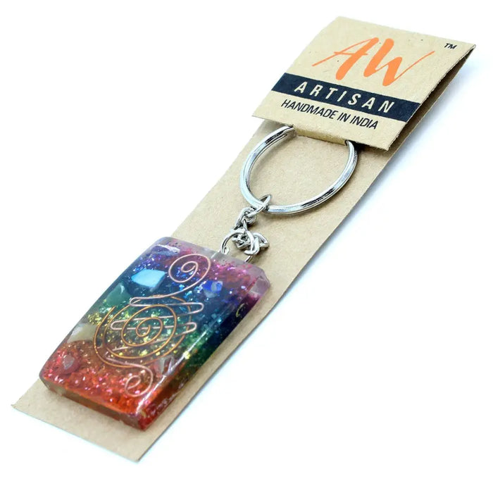 A rectangular rainbow-colored resin orgonite power keyring with a golden spiral design for home protection and chakra balance