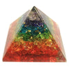 A translucent orgonite pyramid filled with layered colorful chakra gemstone chips in a rainbow gradient