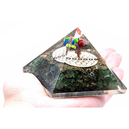 A clear resin orgonite pyramid with green aventurine, gold flecks, colorful beads, and a white flower of life design