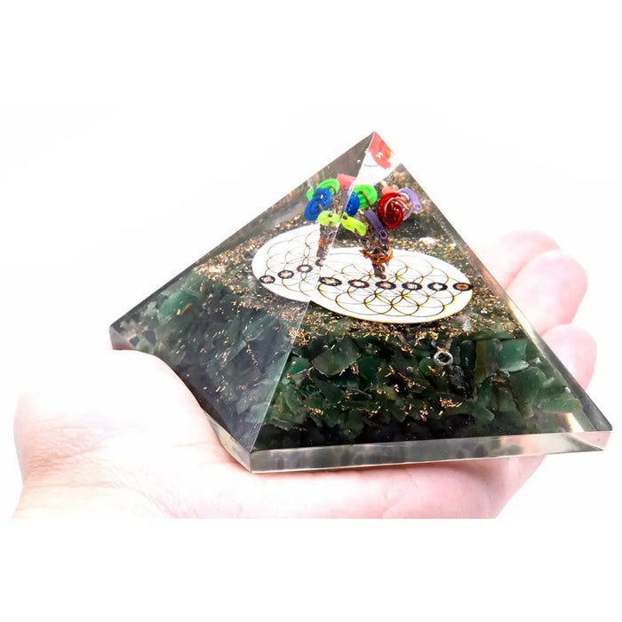A clear resin orgonite pyramid with green aventurine, gold flecks, colorful beads, and a white flower of life design