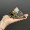 A 5cm orgonite pyramid with black and gold speckled base, colorful chakra symbol, and white quartz crystal top