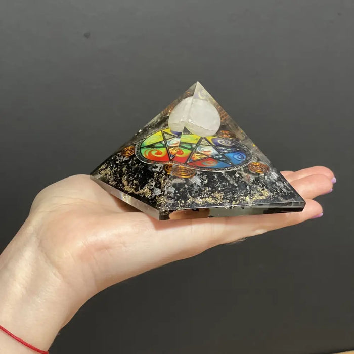 A 5cm orgonite pyramid with black and gold speckled base, colorful chakra symbol, and white quartz crystal top