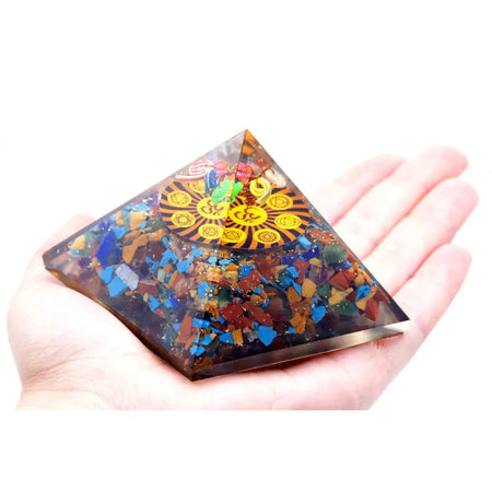 Orgonite pyramid with colorful gemstone fragments in translucent resin featuring a golden om chakra design