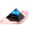 A hand holds a large orgonite pyramid with turquoise chips and black tourmaline with gold threads inside