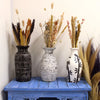 Three ceramic vases with black geometric patterns and bamboo motifs on distressed white and white surfaces on a blue table
