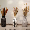 Three cream ceramic vases with black and white patterns holding dried floral arrangements in a simple setting