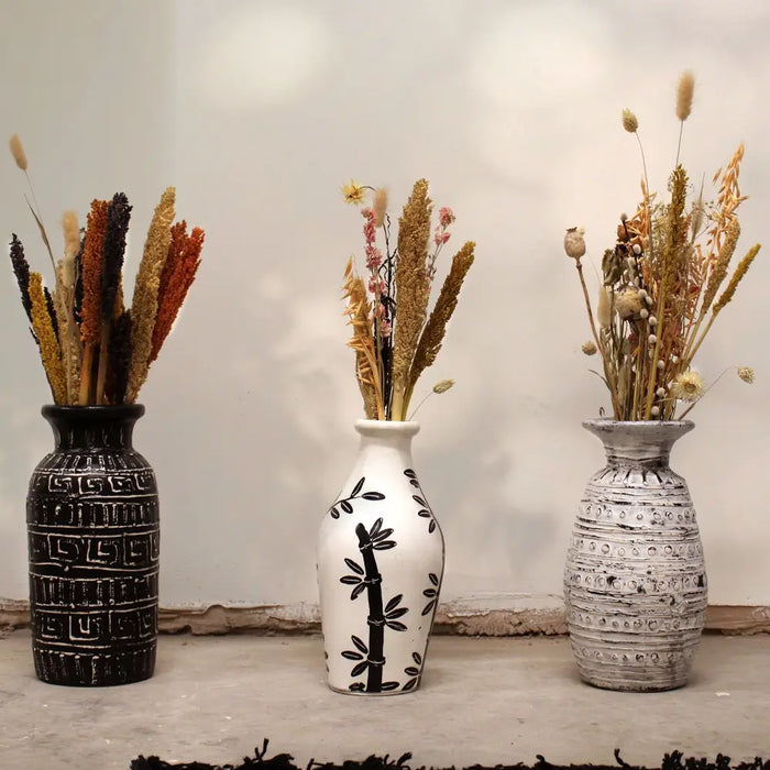 Three cream ceramic vases with black and white patterns holding dried floral arrangements in a simple setting