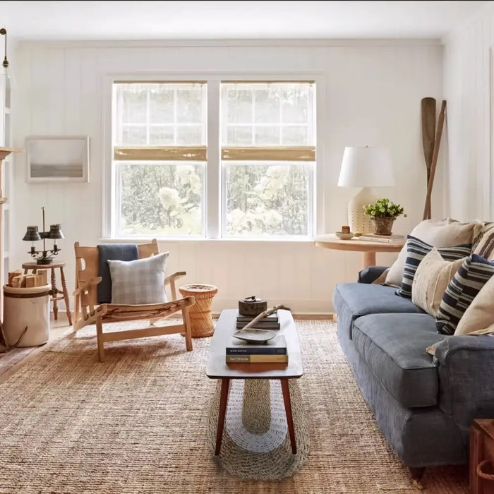 Gray upholstered sofa with striped and solid pillows on a natural and white oval-shaped seagrass rug