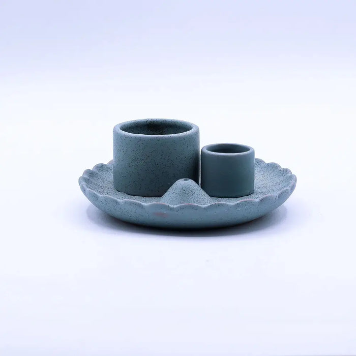 A matte teal ceramic palo santo stick and smudge holder with two cylindrical holders on a scalloped lotus flower base