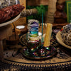 Iridescent metallic rainbow smudge holder holding a wrapped sage bundle and an upright palo santo stick