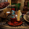 Red ceramic smudge holder with a mandala heart design holding a long palo santo stick and a wrapped sage bundle labeled mexico