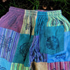 Patchwork trousers in green with purple teal and blue striped panels and black floral embroidery inspired by mushroom tones