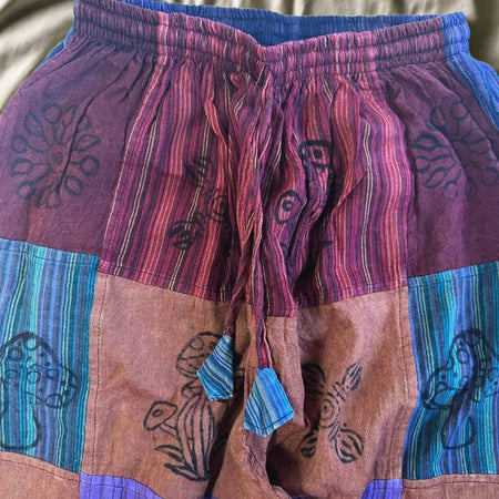 Patchwork trousers in purple with vibrant stripes and black floral embroidery featuring a subtle mushroom motif