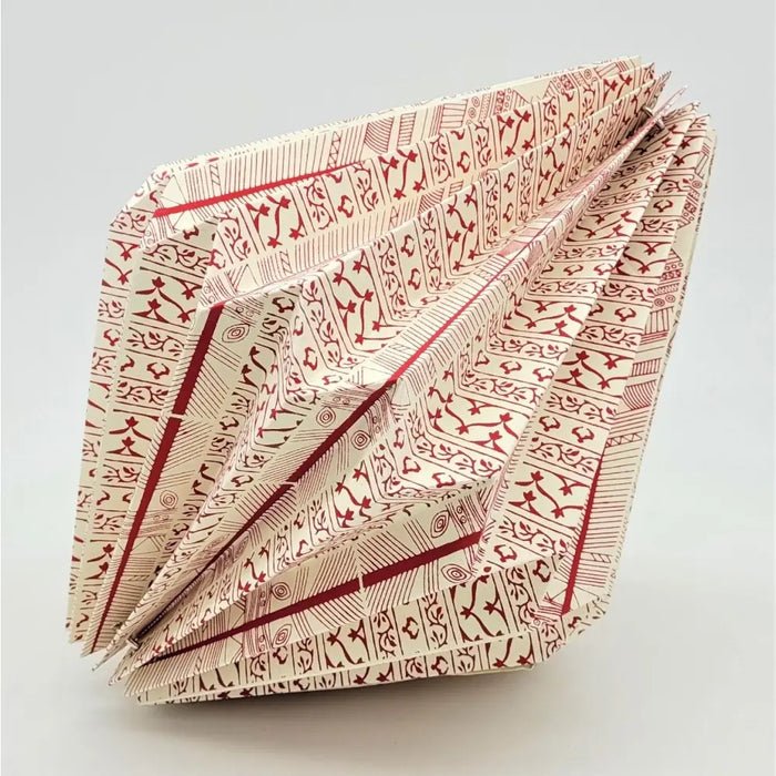 A cream-colored patterned origami light shade with red geometric designs folded into sharp creases for a short pendant
